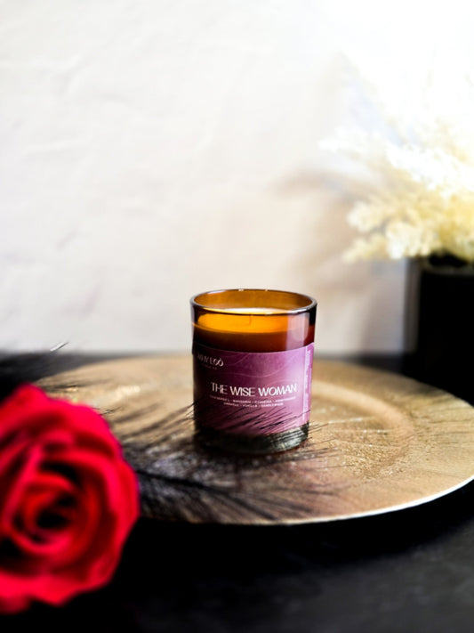 Candle labeled 'The Wise Woman' on a wooden surface with a red rose in the foreground.
